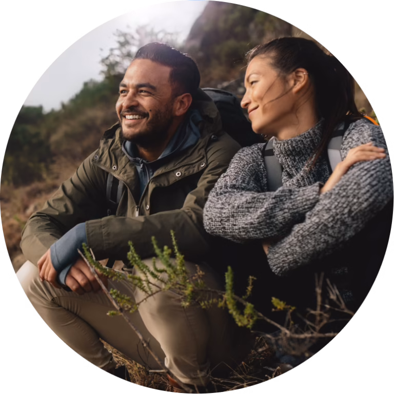 Two hikers sitting together on a hillside, smiling and looking out at the view
